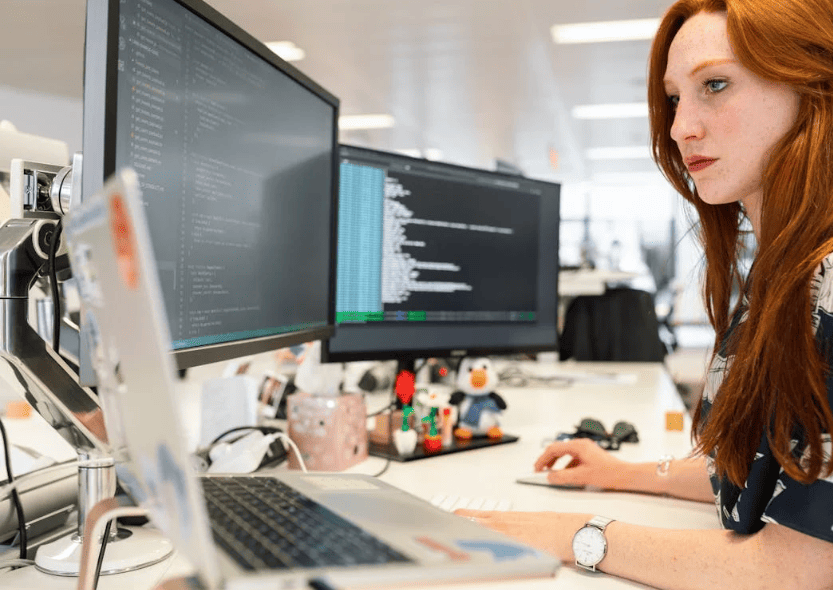 A woman with two desktop screens and a laptop working at desk.