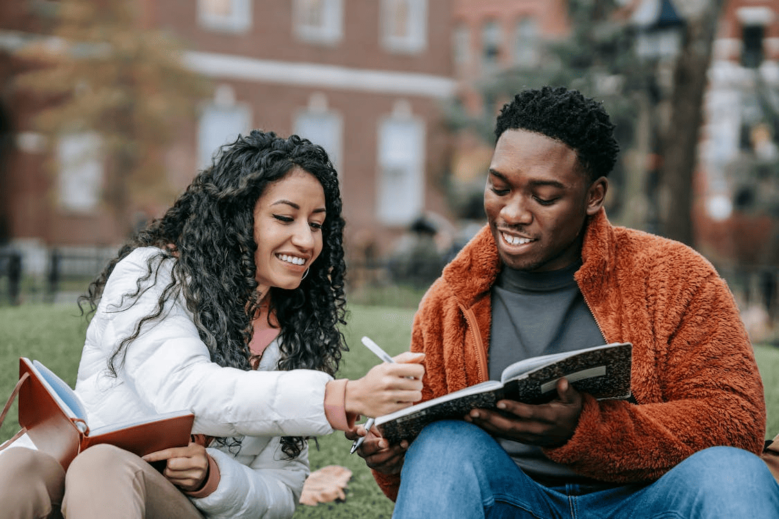 College students working with pen and notebooks outdoors. 