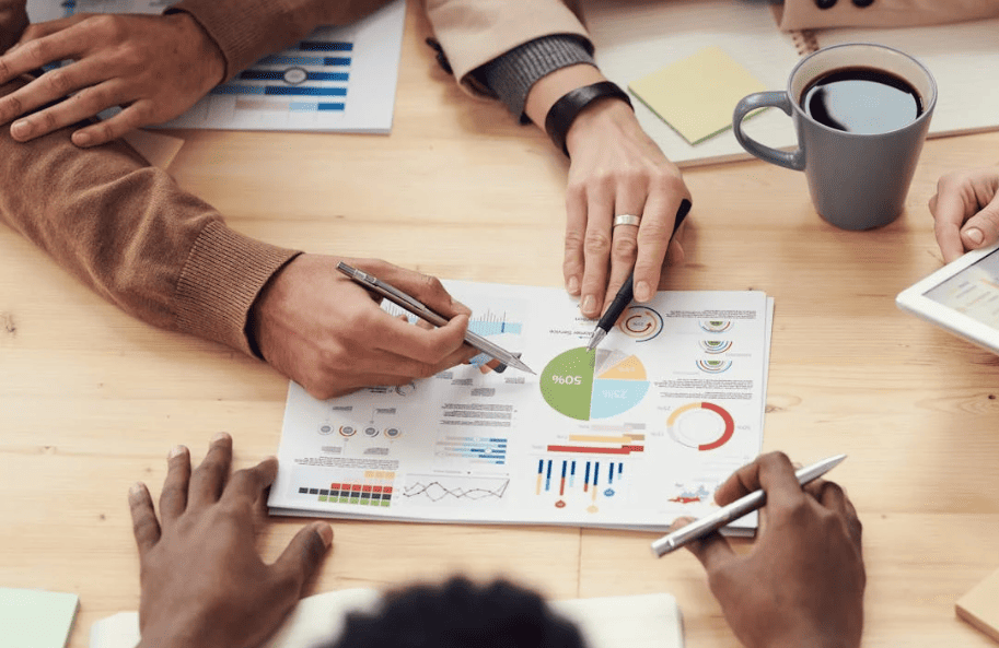 People sitting around at table and looking at graphs while holding pens. 