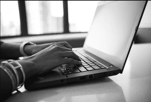 A balck and white image of a person typing on the keyboard of a laptop.