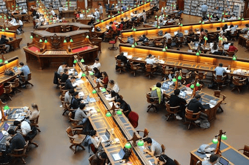 Several tables filled with students in a circular set up in a library. 