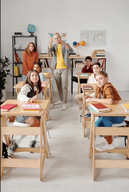 A teacher in a classroom with students sitting in a row of desks.