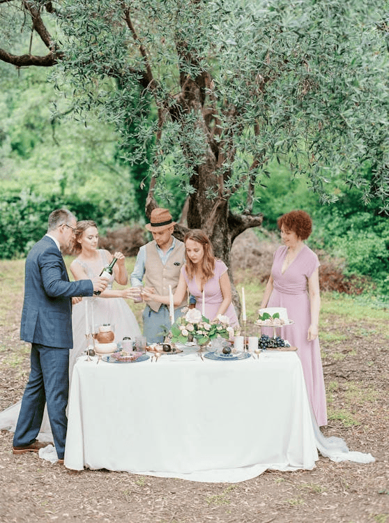 People standing around a table with a white tablecloth and looking at the items on the table.