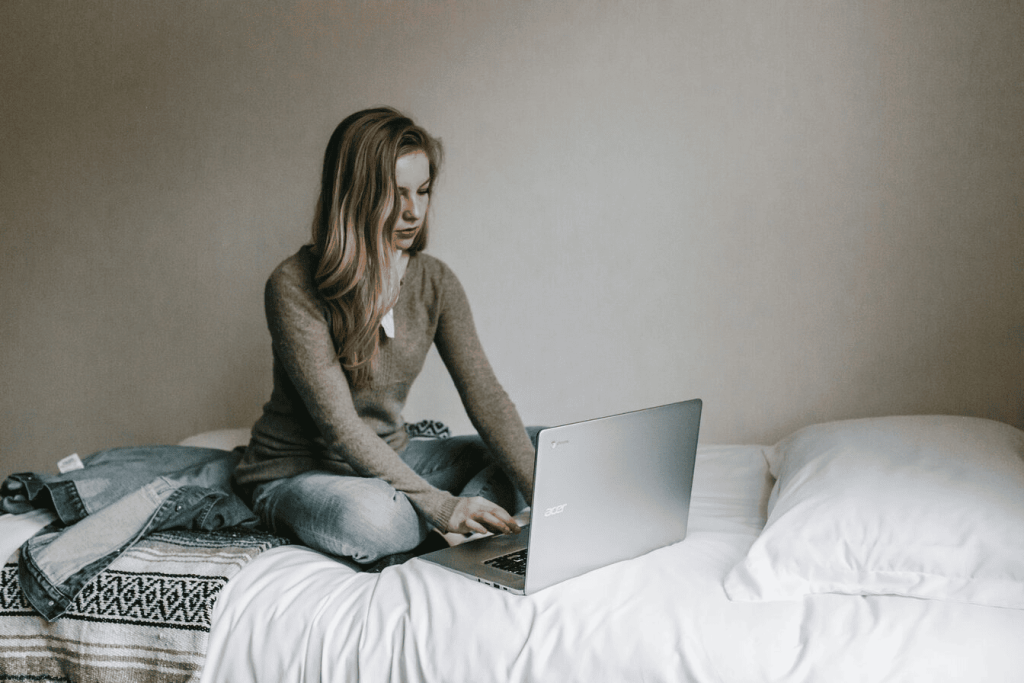 A woman typing on MacBook Pro while sitting on her bed in a room