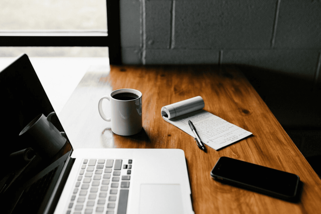 A MacBook Pro, white ceramic mug, and black smartphone on a table