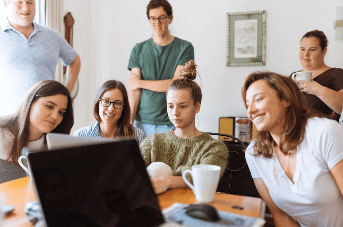 A group of students and a teacher looking at a laptop.