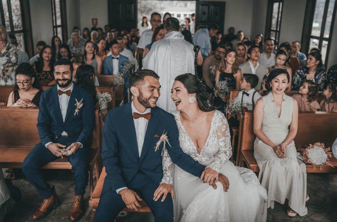 A couple getting married sitting at the front of the church with their guests behind them.