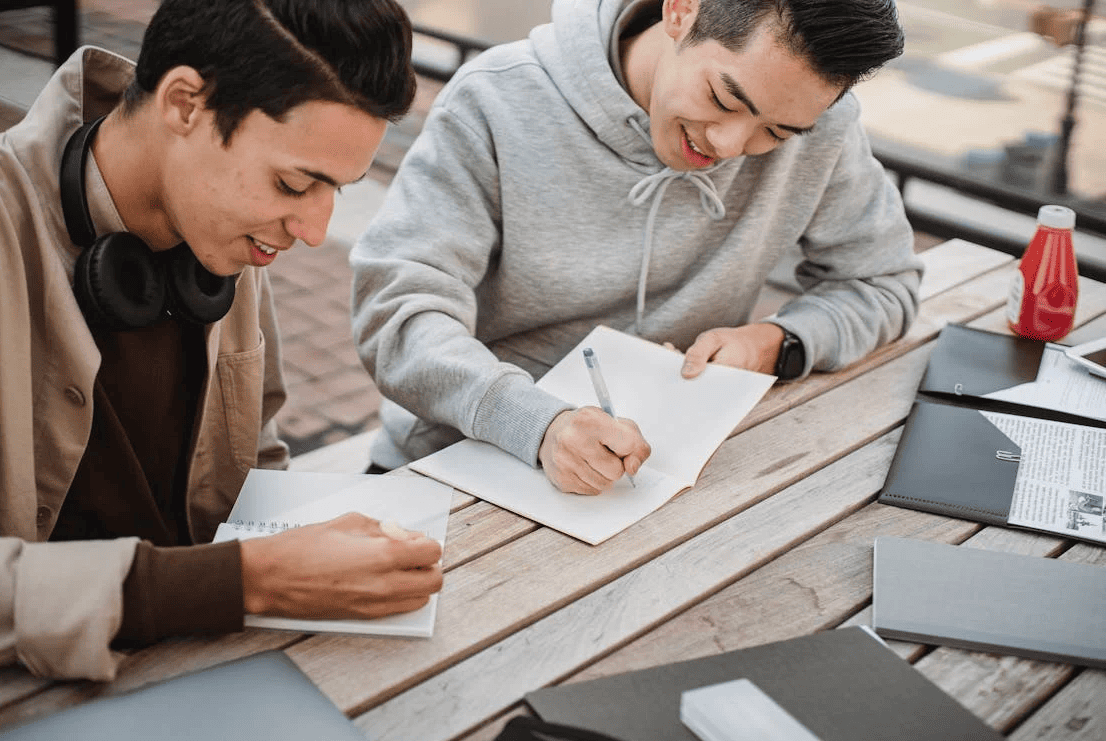 Two people writing in their notebooks and smiling.