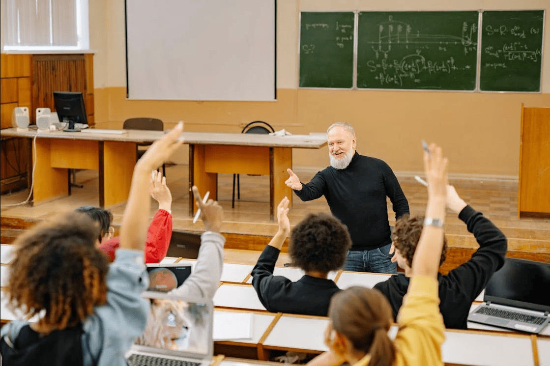 Students raising their hands in class in front of a professor. 