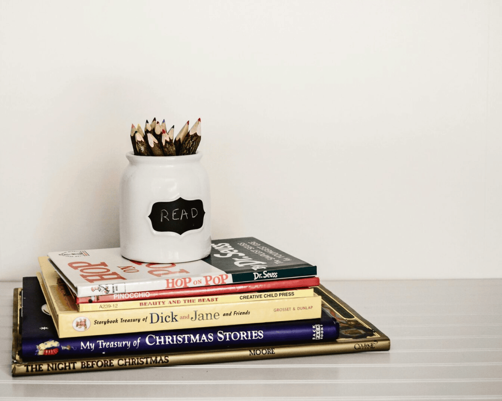 A white ceramic pencil organizer on top of stack of books.