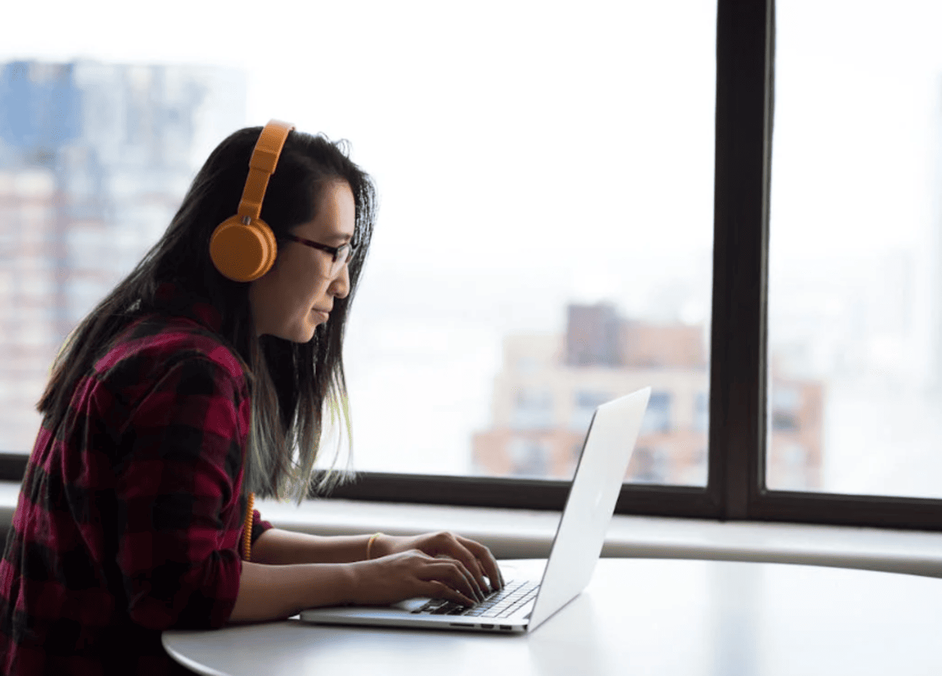 A woman with orange headphones typing on a laptop. 