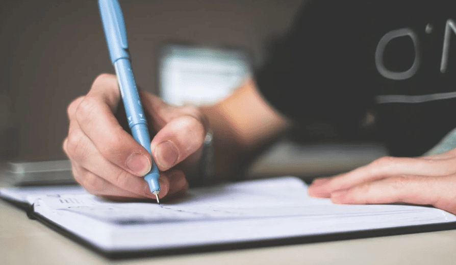 A person writing with a blue pen in a notebook.