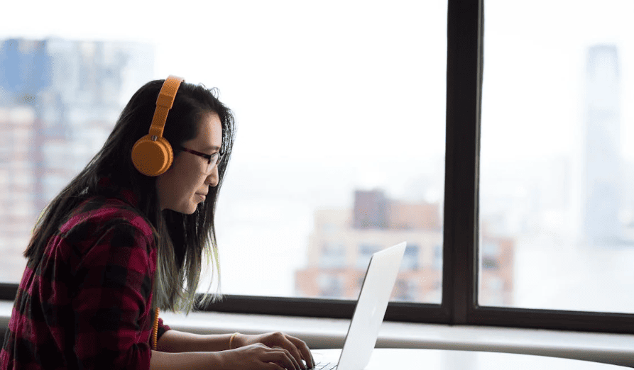 A person typing on a laptop with orange headphones on. 