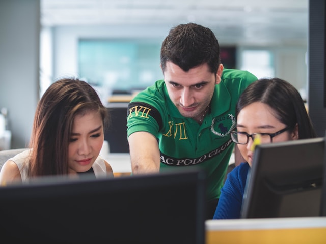 Two students with a lecturer looking at their computer screens. 