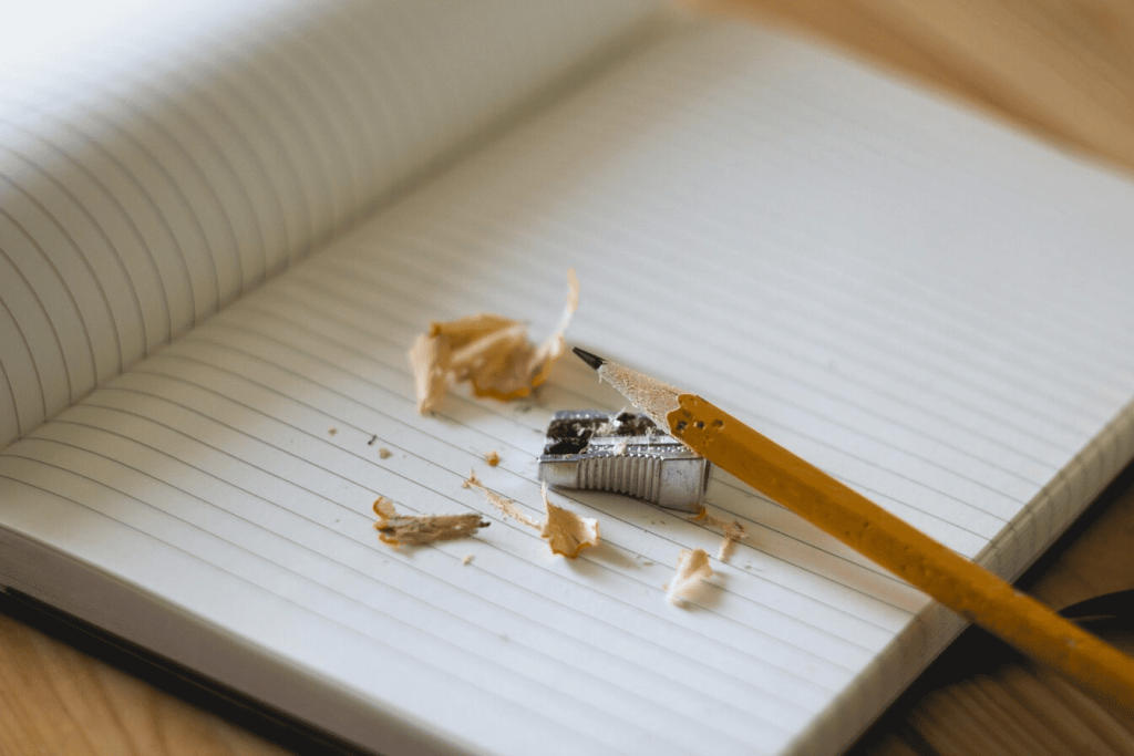 A pencil and sharpener on a notebook page with pencil shavings scattered on the page.