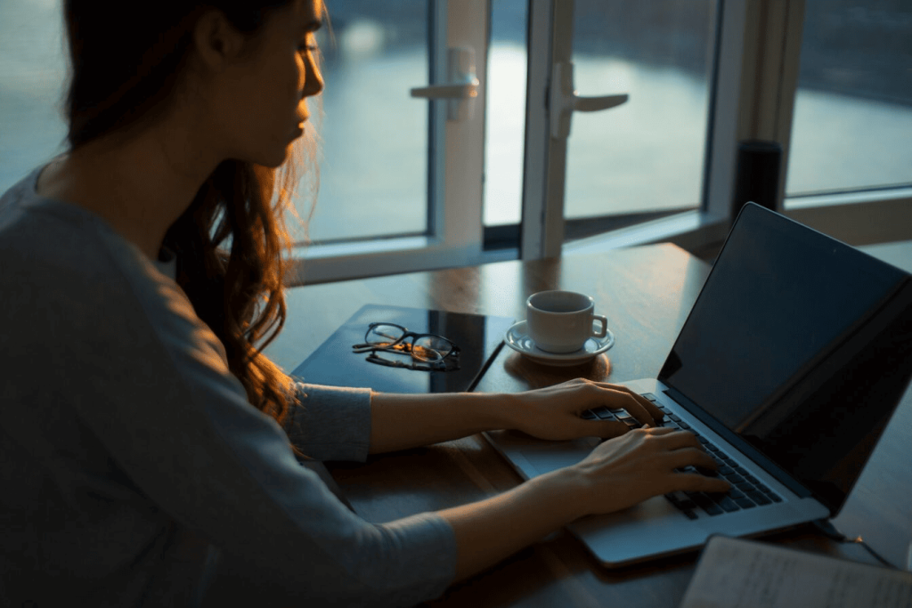 A woman sitting at a desk next to an open window and working on her laptop.