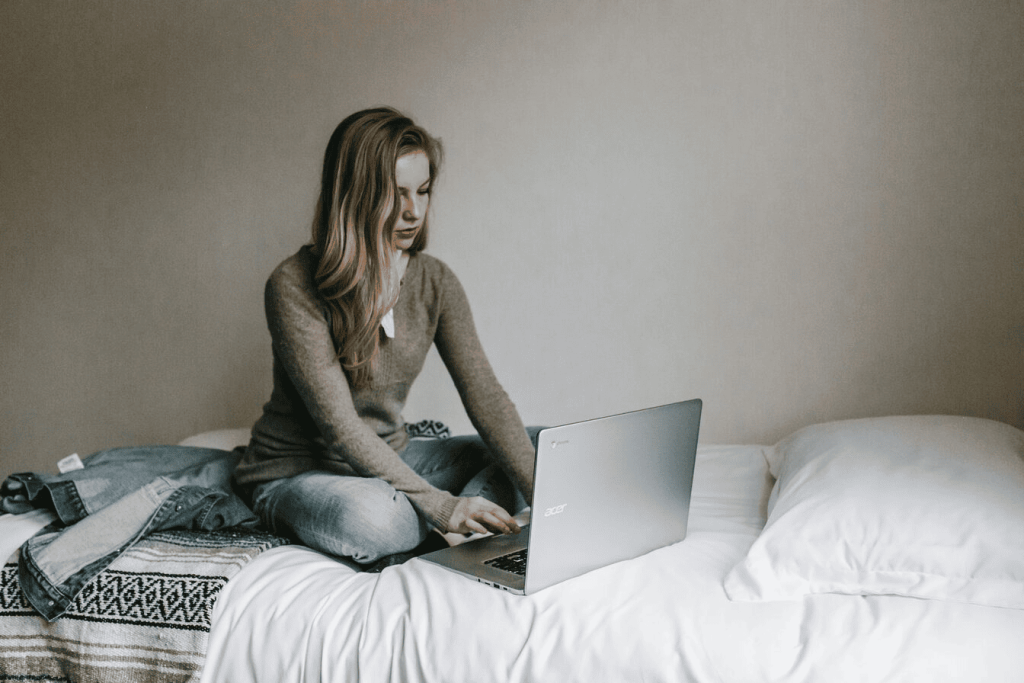 Een vrouw typt op MacBook Pro terwijl ze op bed in kamer zit.