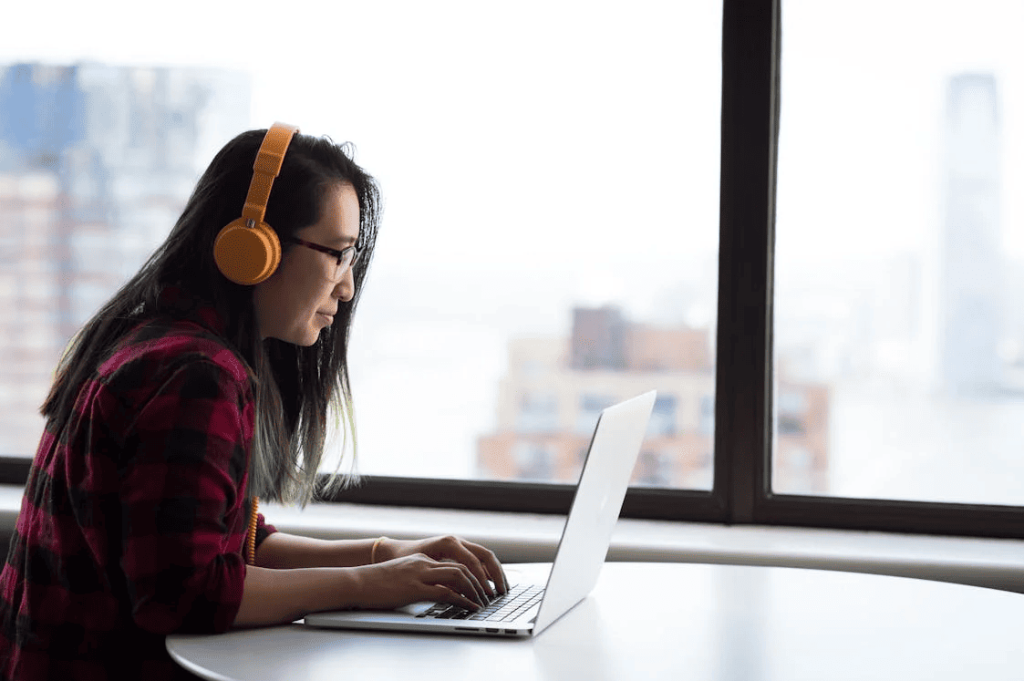 A person typing on a laptop while wearing orange headphones. 