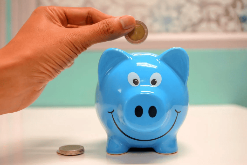 A person putting a coin into a blue piggy bank. 