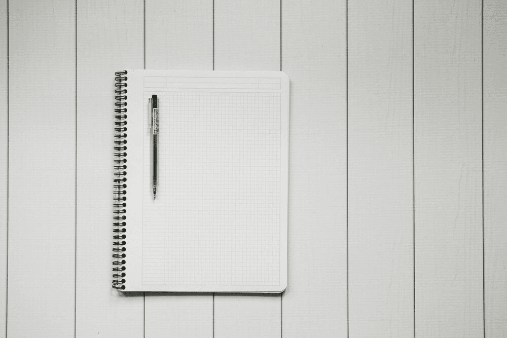 A notebook with a pen on top of it on white table.