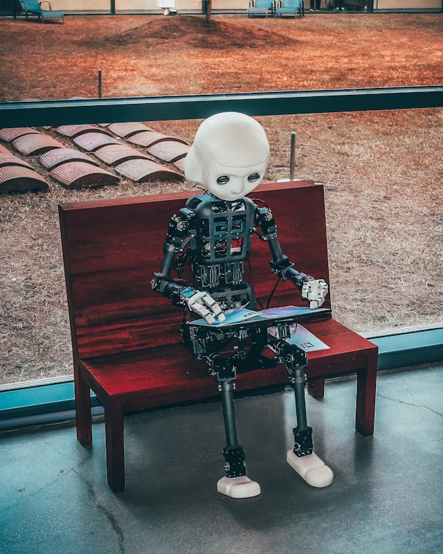 A robot sitting on a bench reading a magazine. 