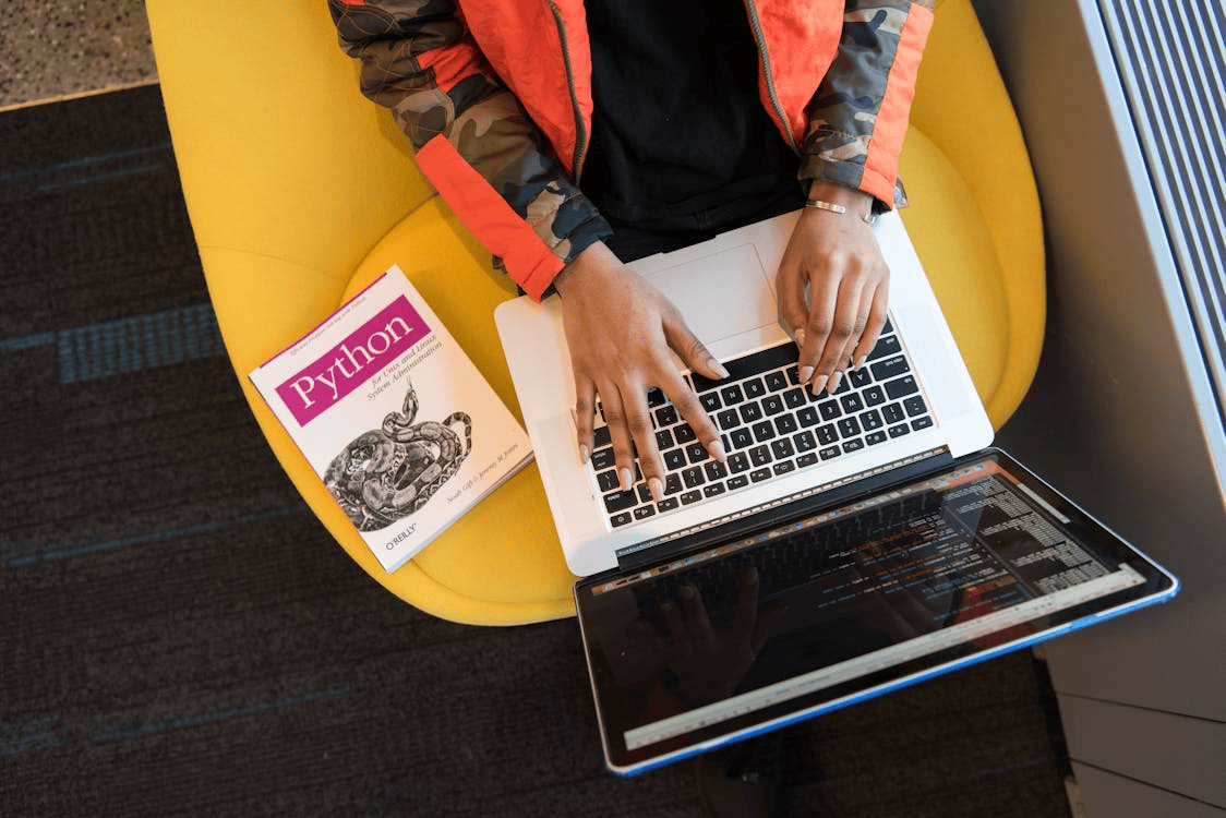 Une personne utilisant un ordinateur portable avec un livre sur Python à côté d'elle.