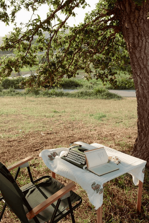 Une machine à écrire à l'ancienne avec un livre appuyé dessus sur une table à l'extérieur.