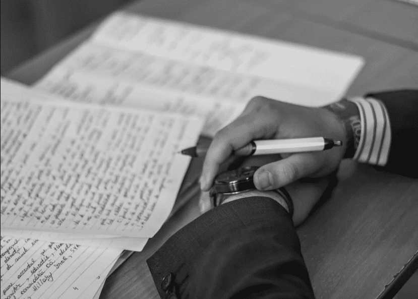 Photo en niveaux de gris d'une personne tenant un stylo à côté d'un cahier.