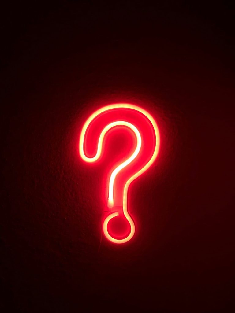Un point d'interrogation en néon sur fond sombre. 