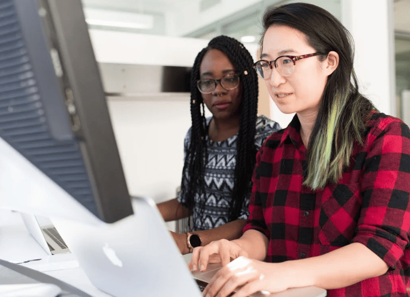 Two women looking at a computer screen and laptop.