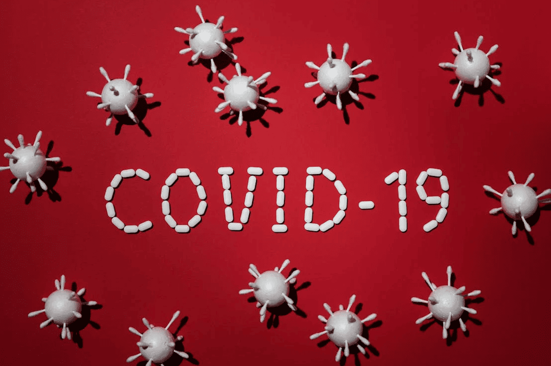 The phrase "COVID-19" surrounded by images of small viruses on a red background. 