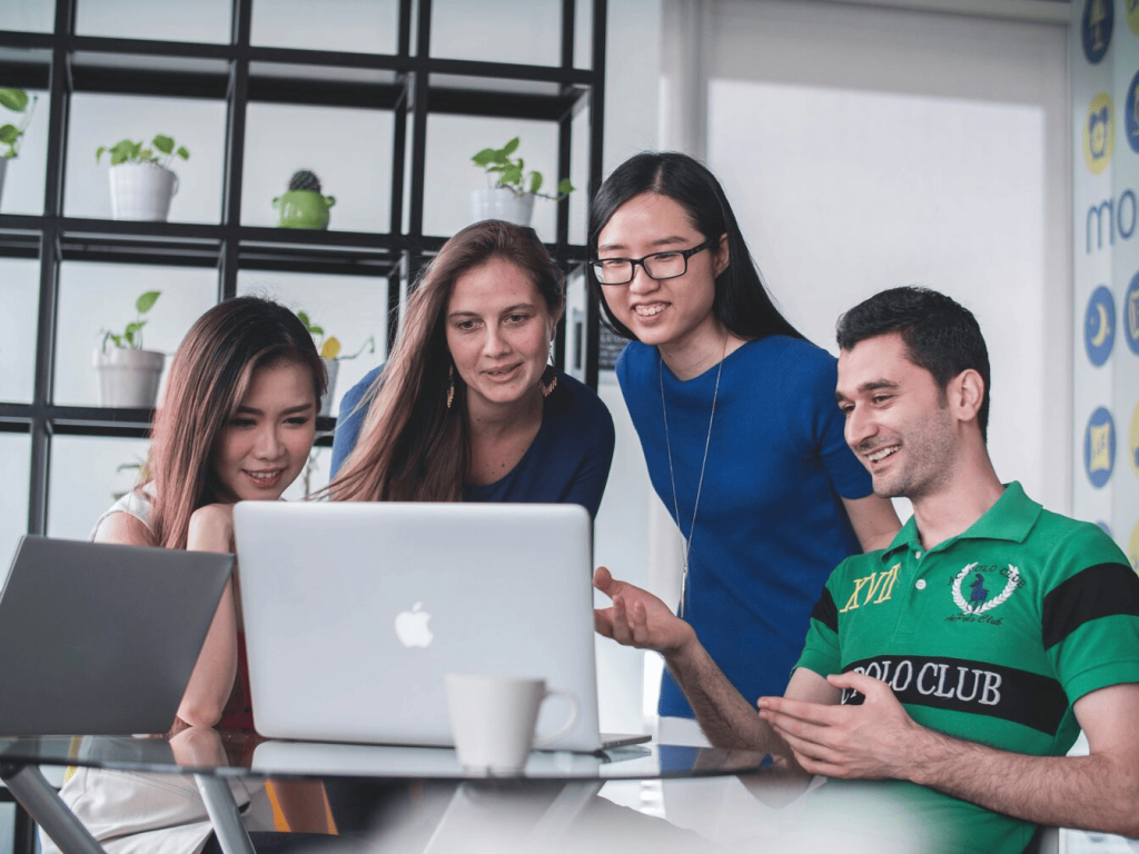 Four people looking at a MacBook Pro and smiling.