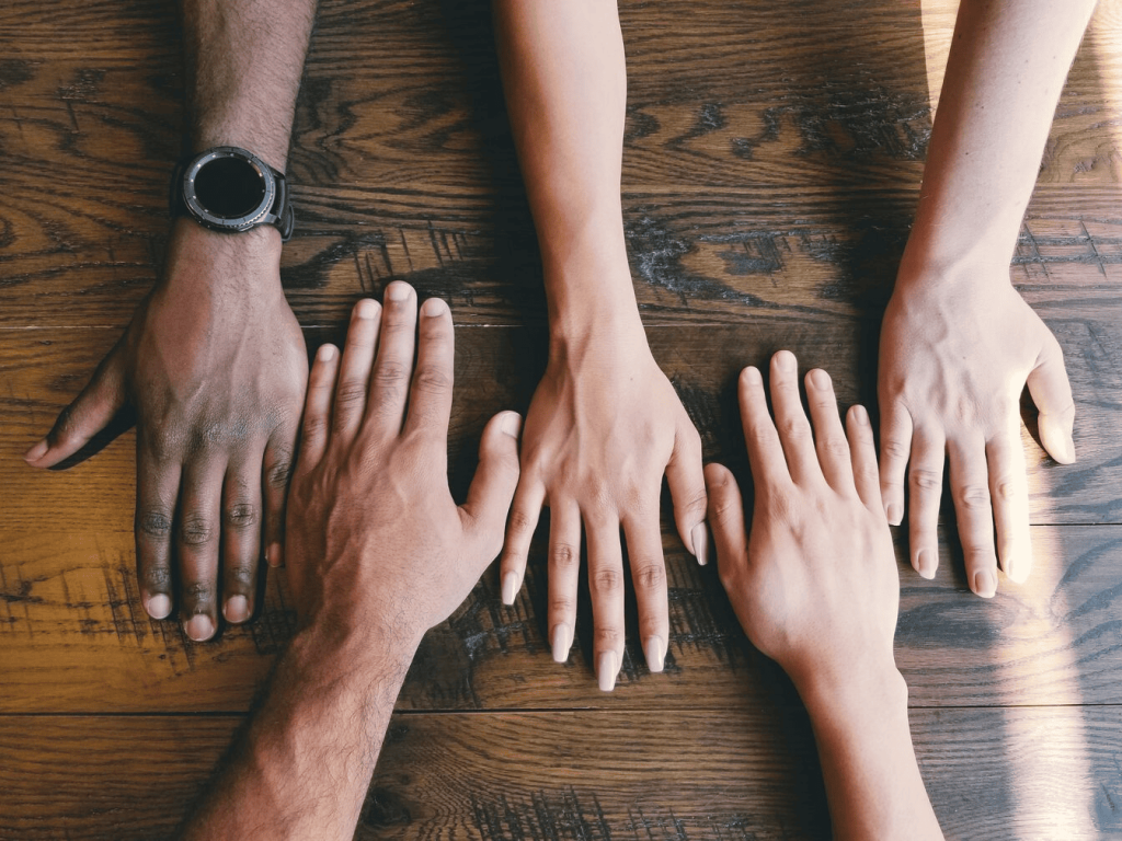 Five human hands next to each other on a brown surface.