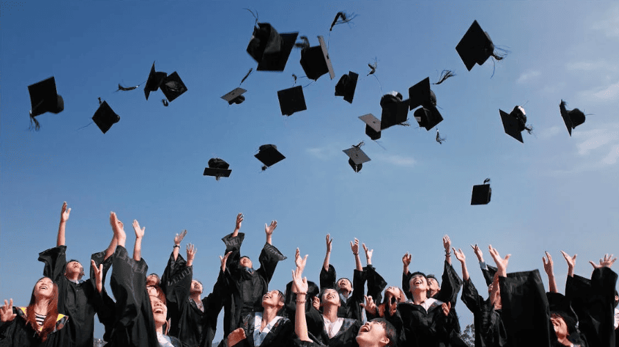 Students with graduation gowns throwing their hats into the air.