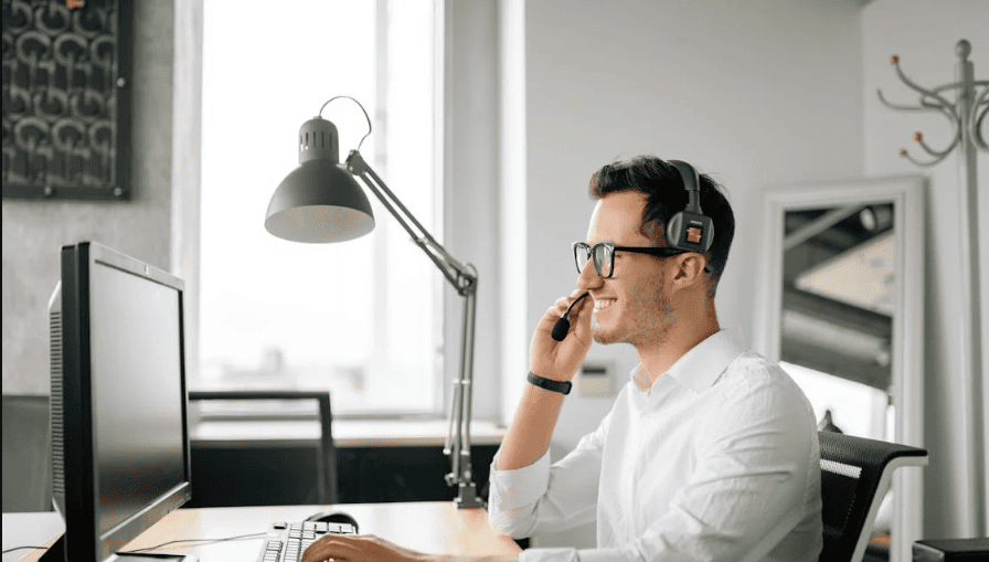 A man sitting in front of a monitor with a headset. 