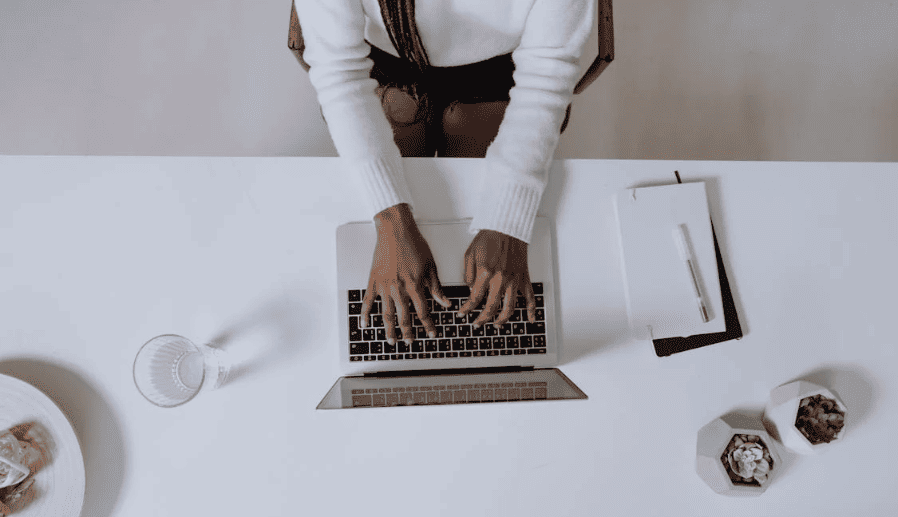 A person typing on a laptop on a white table. 