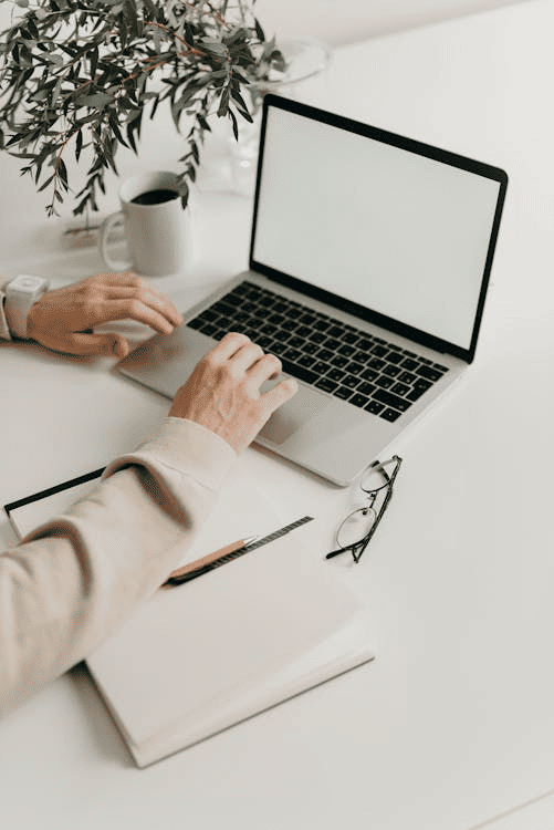 A person typing on a laptop on a white table. 