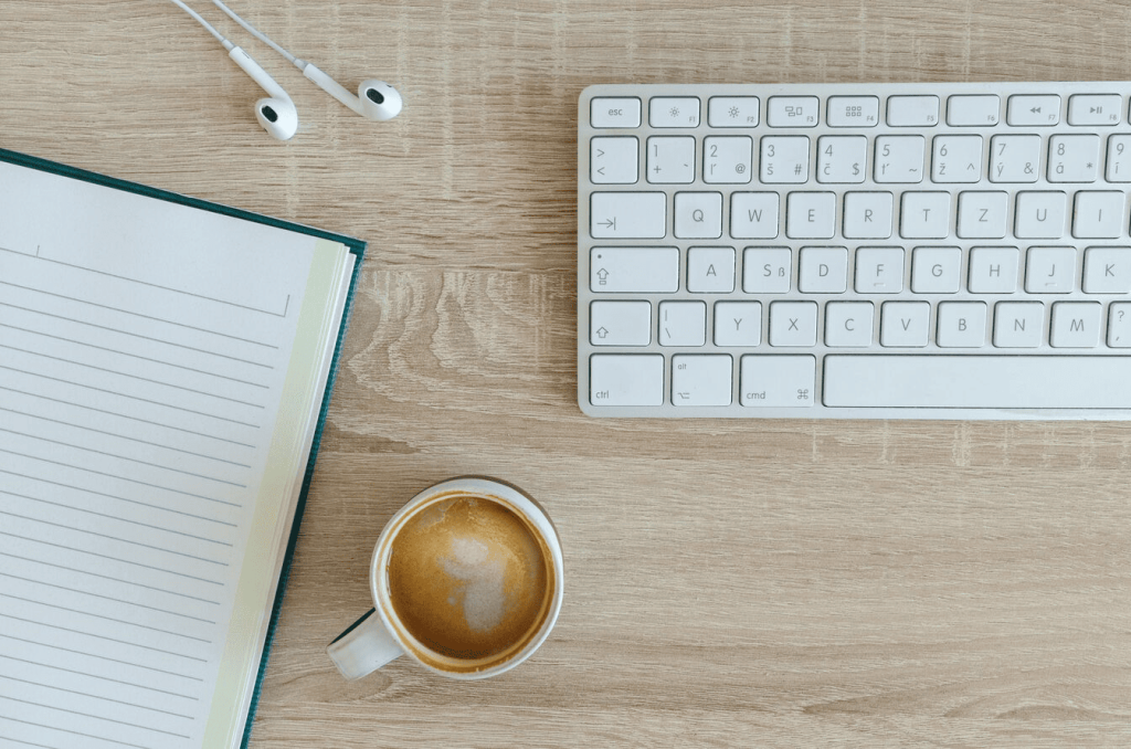 A cup of coffee near a white wireless keyboard and Apple EarPods.