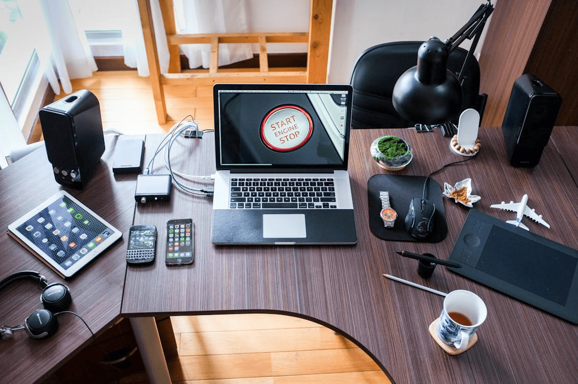 A laptop, tablet, smartphones, speakers, and other items on top of a wooden desk.