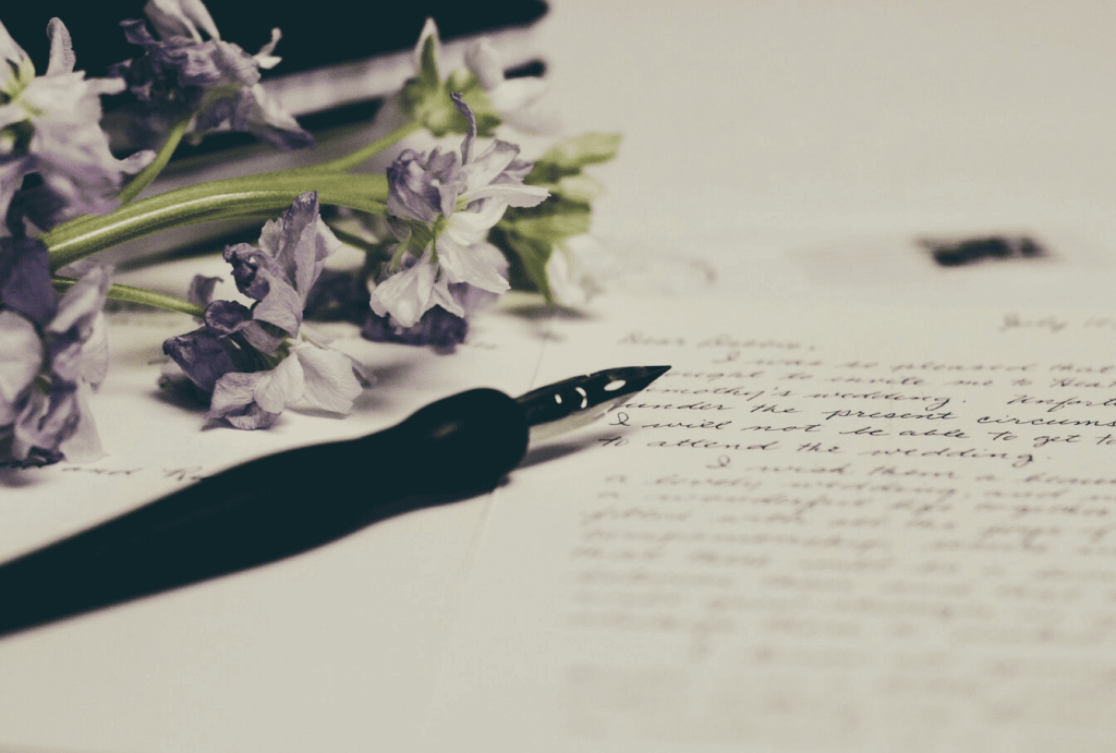 Purple flowers on paper next to a fountain pen and a piece of paper.