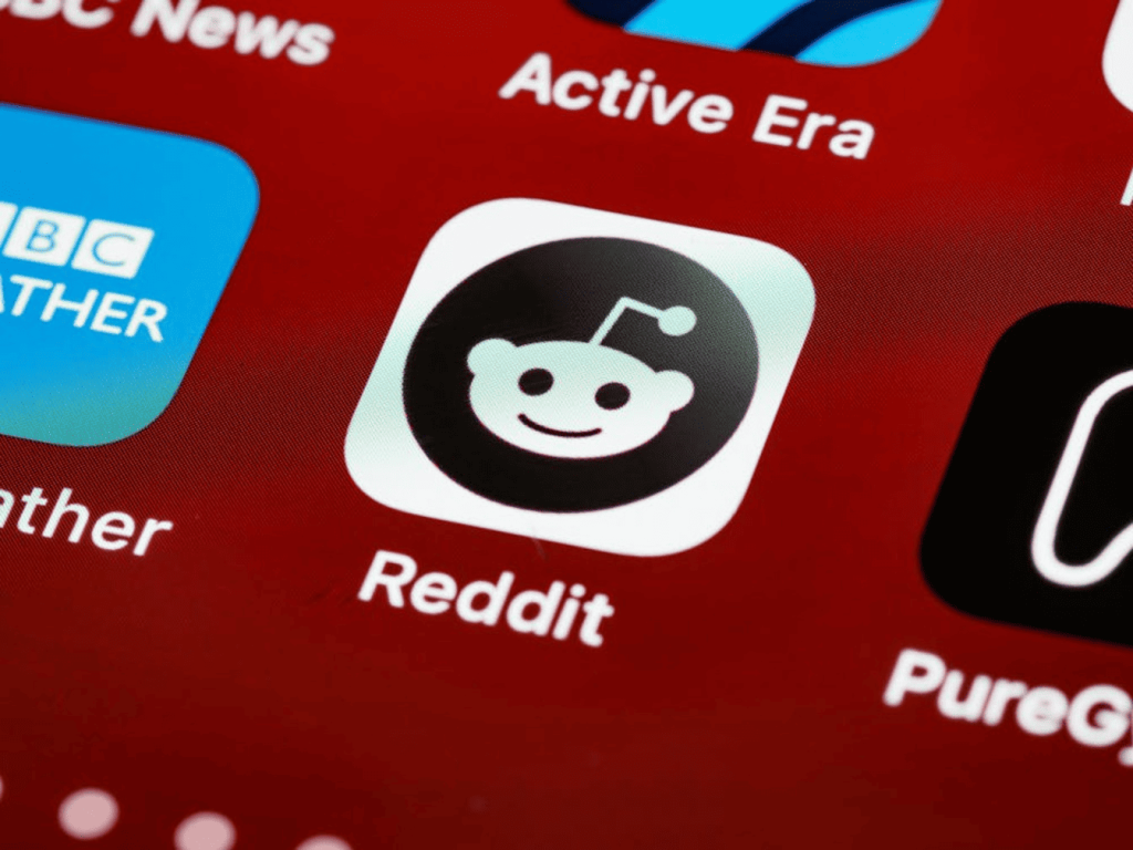 Aplikasi Reddit yang ditampilkan pada layar smartphone dengan latar belakang merah. 