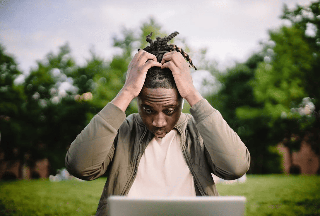 A man upset and holding his hair while looking at a laptop screen. 