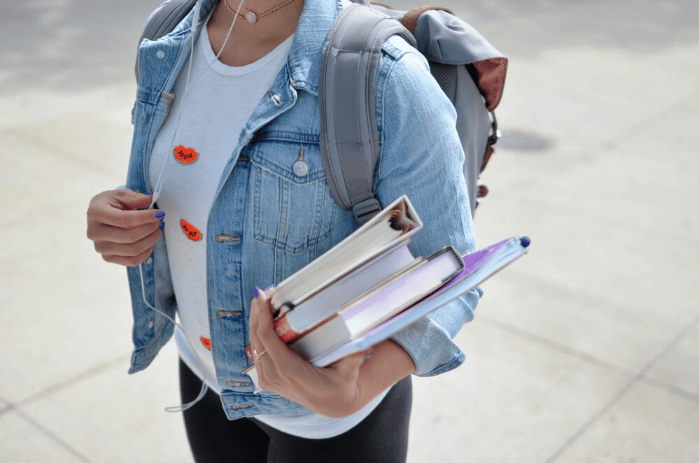 A woman wearing blue denim jacket while holding books.