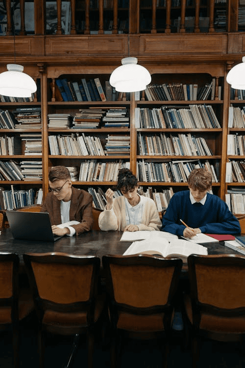 Students working in a library with book shelves behind them.