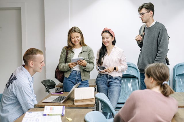 A group of students gathered around a desk, discussing essay topics and studying.