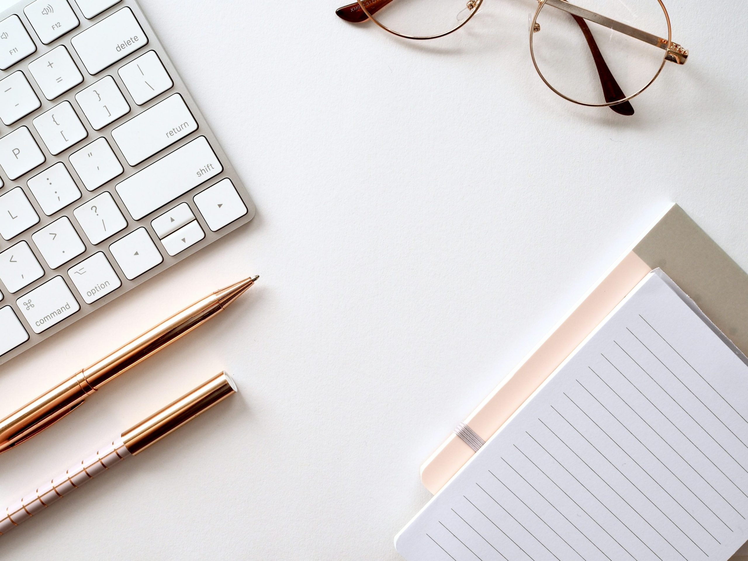 A pen and pencil near a keyboard, reading glasses, and a notebook.