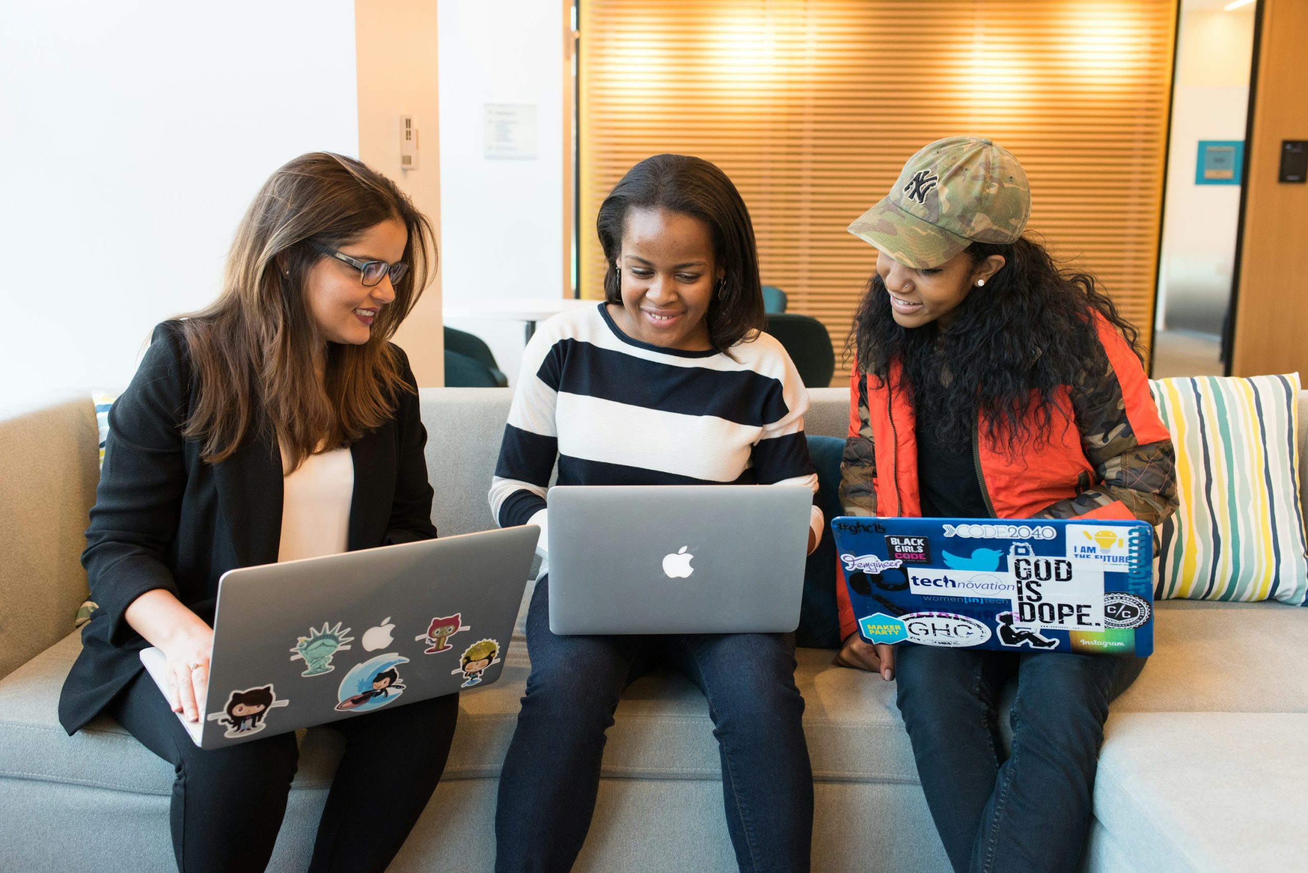 Three women sitting on sofa with MacBook.