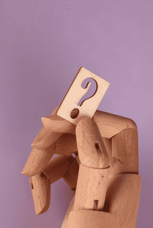 A wooden hand holding a question mark with a purple background. 