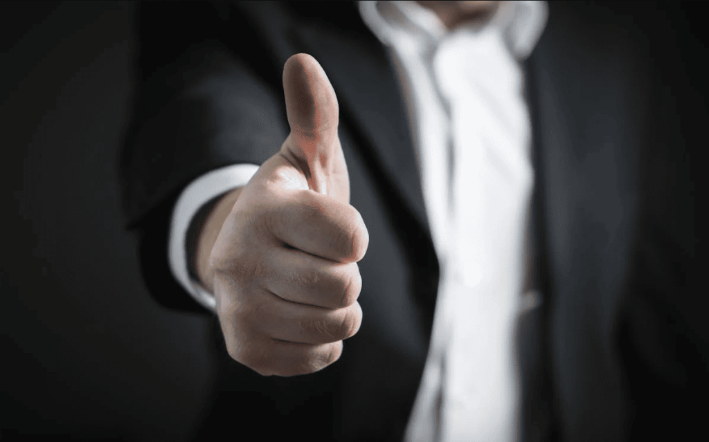 A close up of a man in a suite doing a thumbs up. 