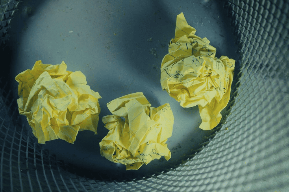 Three yellow crumbled papers inside a gray trash bin.